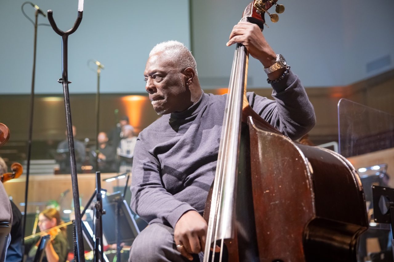 A man rests his hand on a double bass while he prepares to play.
