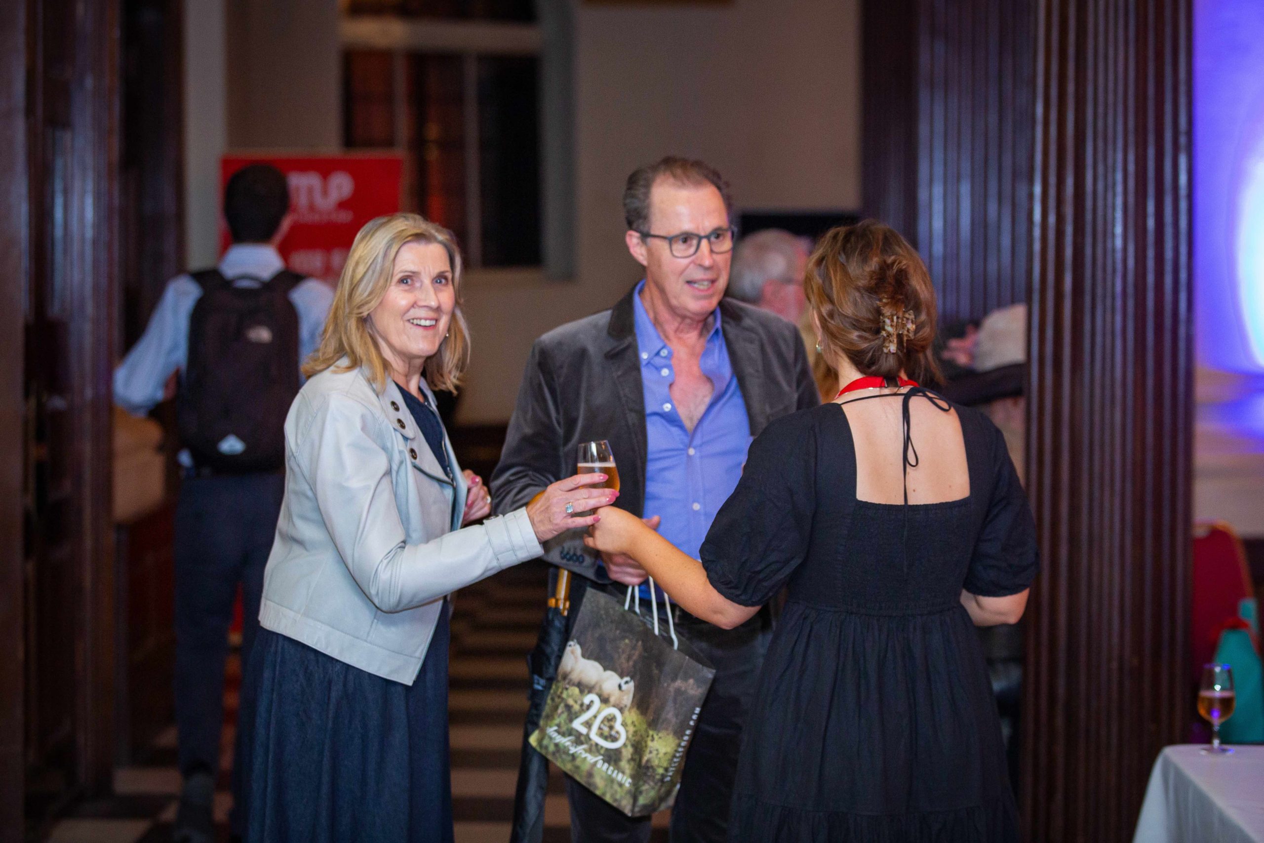 A woman is handed a glass of wine as she looks at the camera.