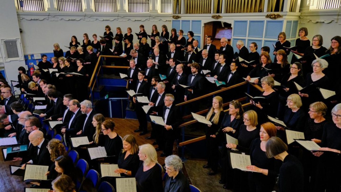 A choir perform wearing black in front of an organ.