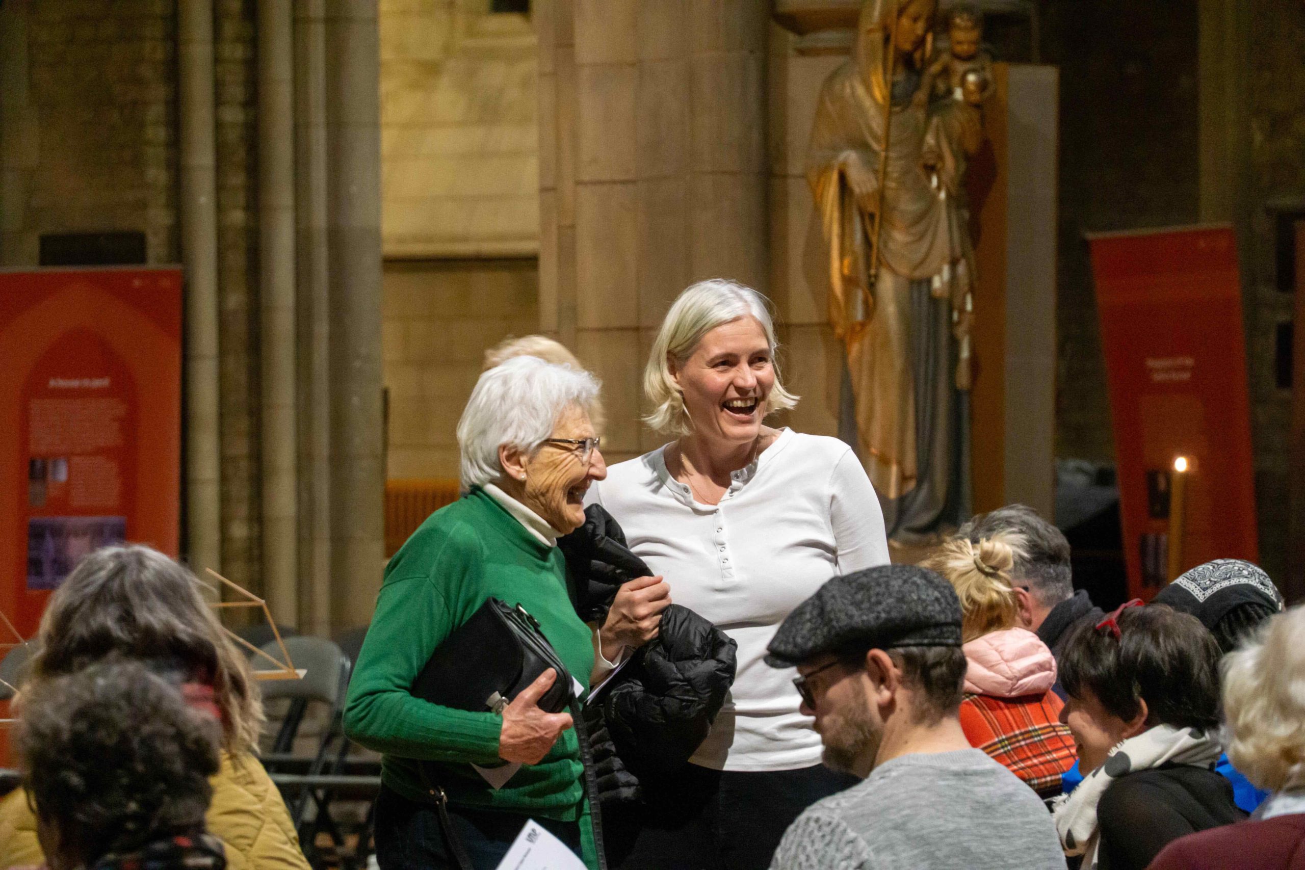 Two women share laughter together standing in the audience.