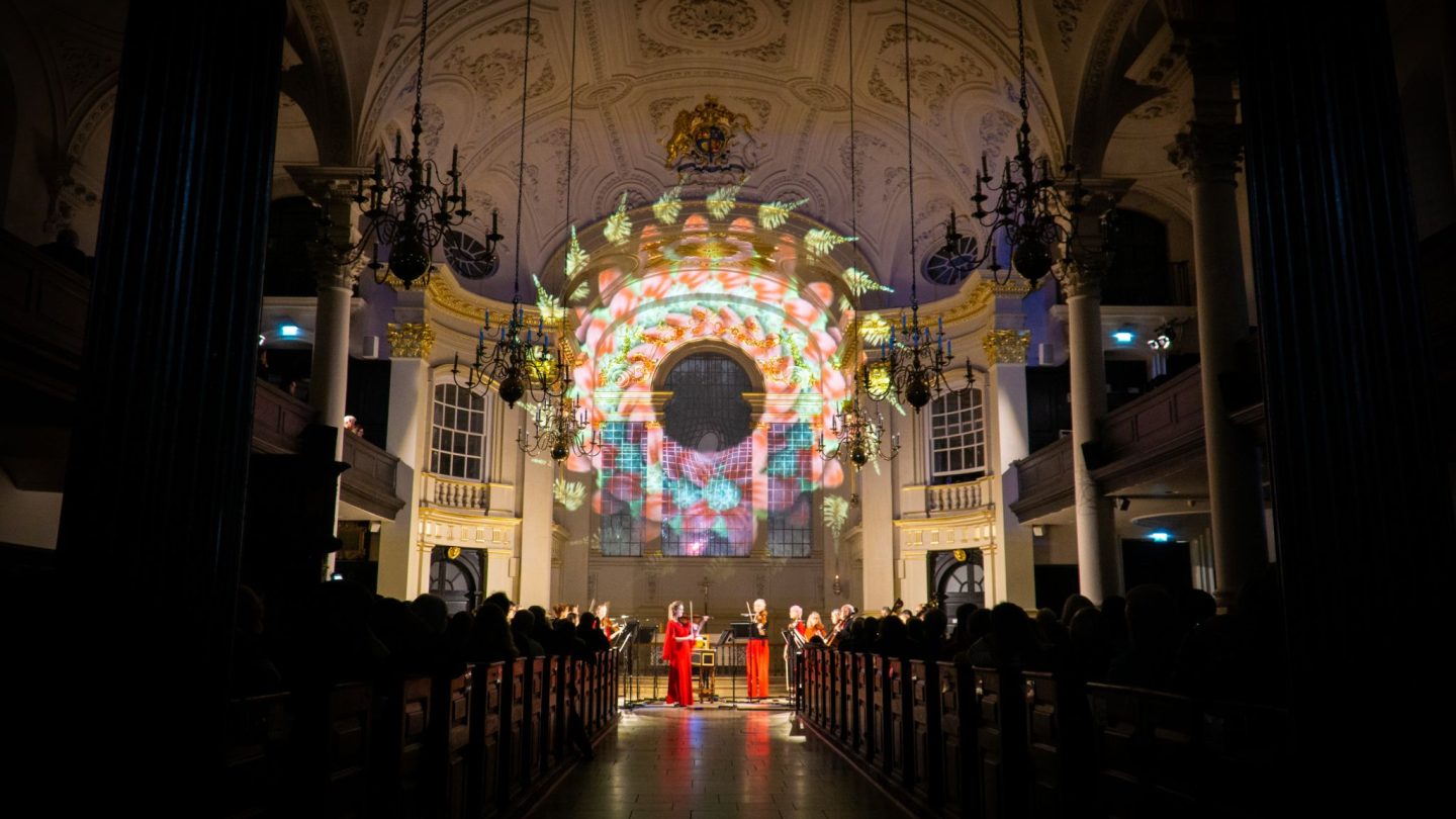 Beautiful lighting projected on the back wall of a church, with performers underneath.