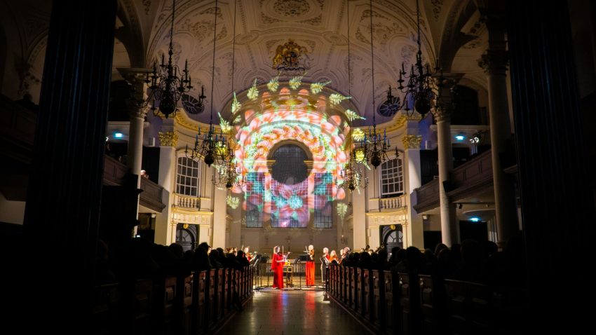 Beautiful lighting projected on the back wall of a church, with performers underneath.