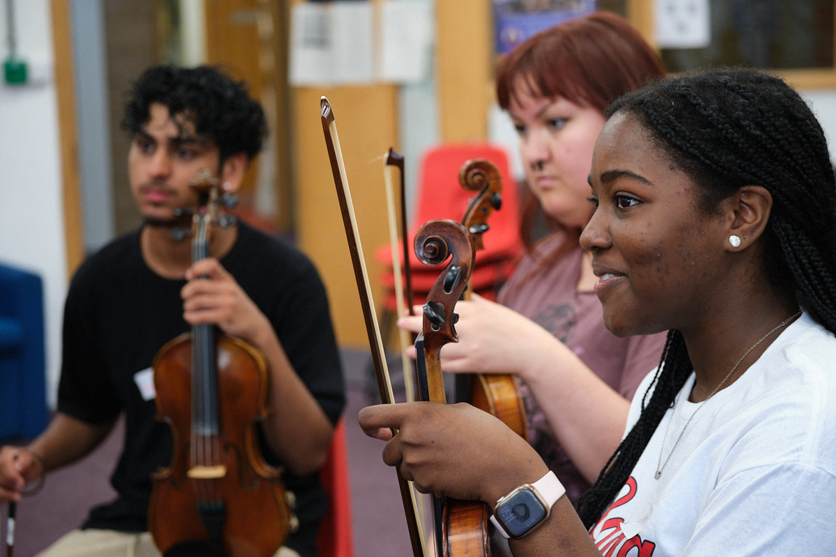 Teenagers sit together holding their violins.