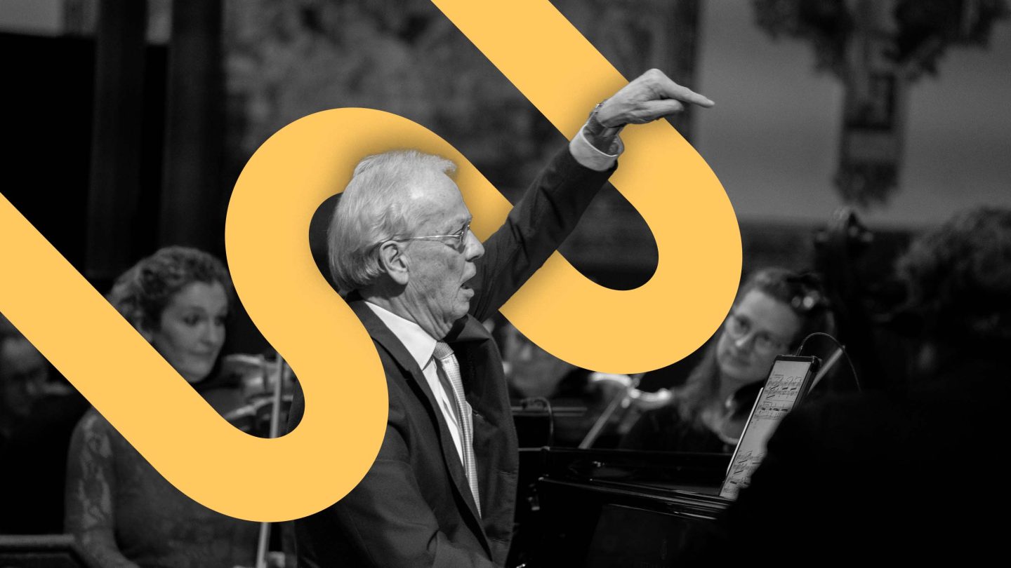 A black and white image of a man raising his hand to conduct with an orange graphic meandering around him.