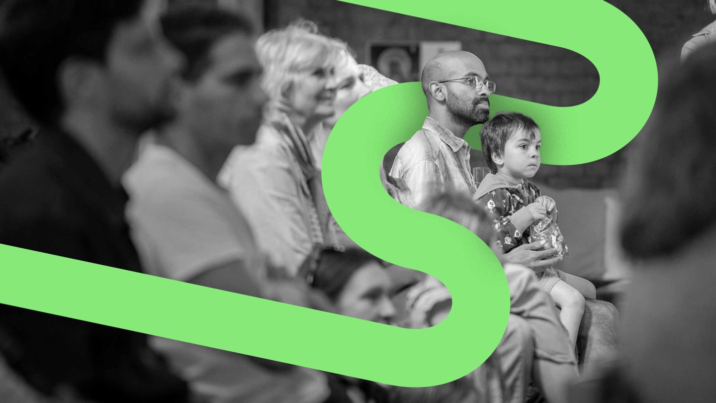 Black and white image of a small child sitting on a man's lap with a green graphic swirling around them.