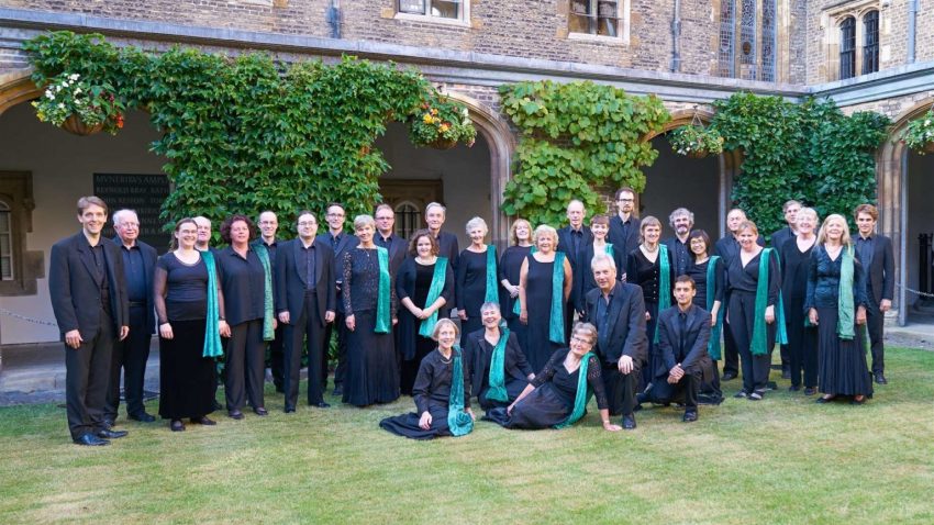 A group of adults pose outside wearing black with turquoise sashes.