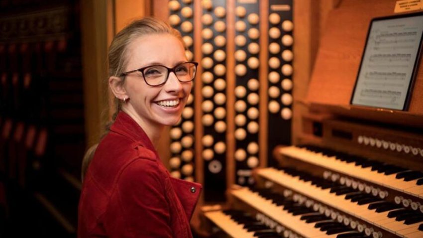 Smiling woman sits in front of an organ console.