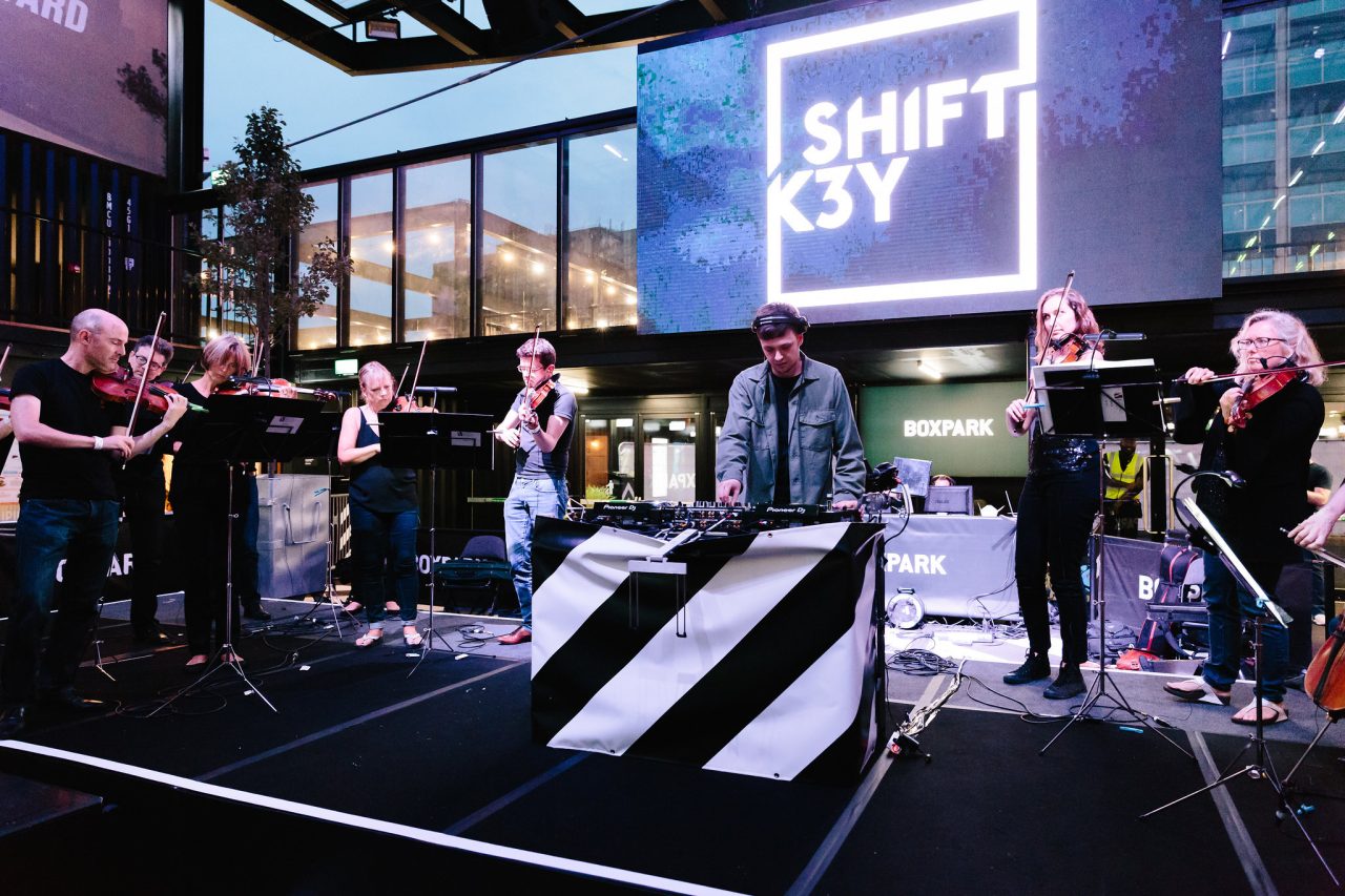 A man with headphones DJs with musicians around him.