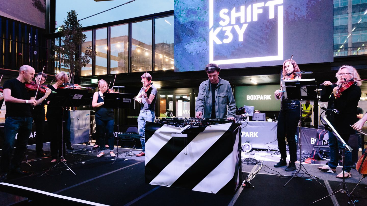 A man with headphones DJs with musicians around him.