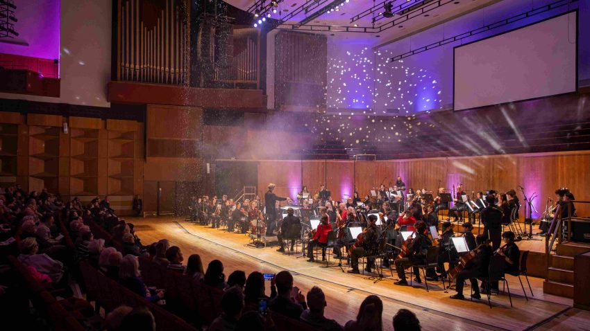 Orchestra on stage with projections creating a sparkling effect.