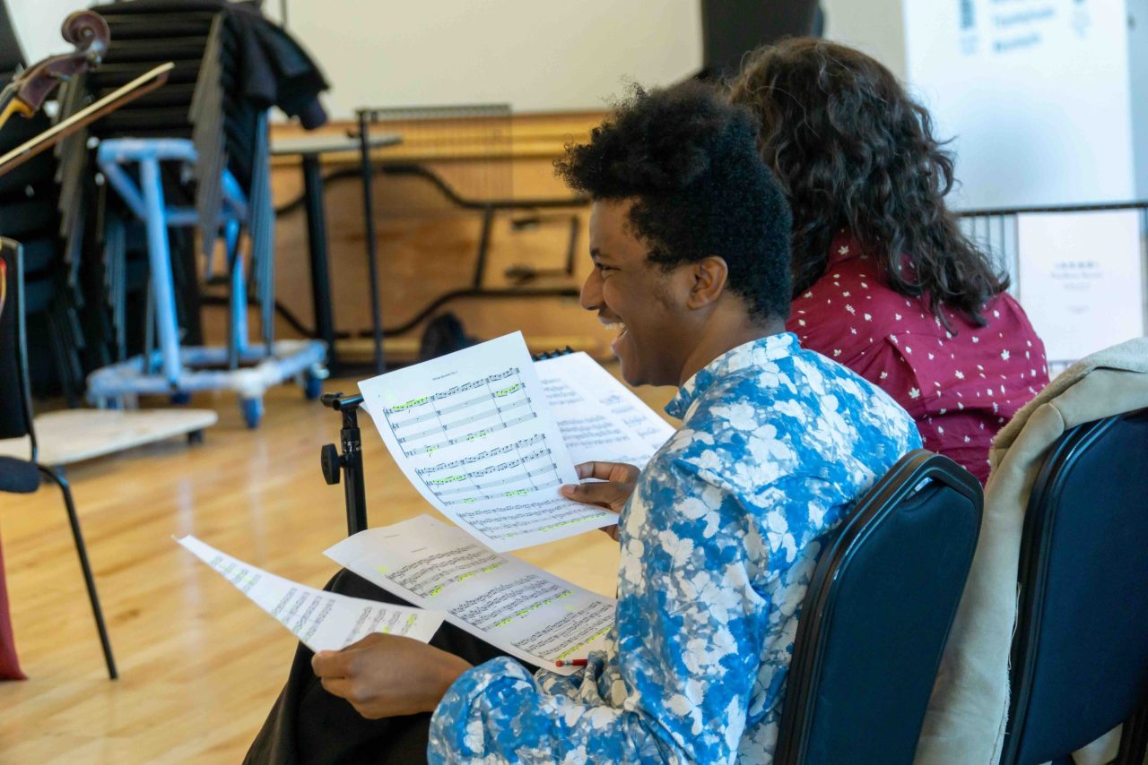 A man laughs while holding sheet music.