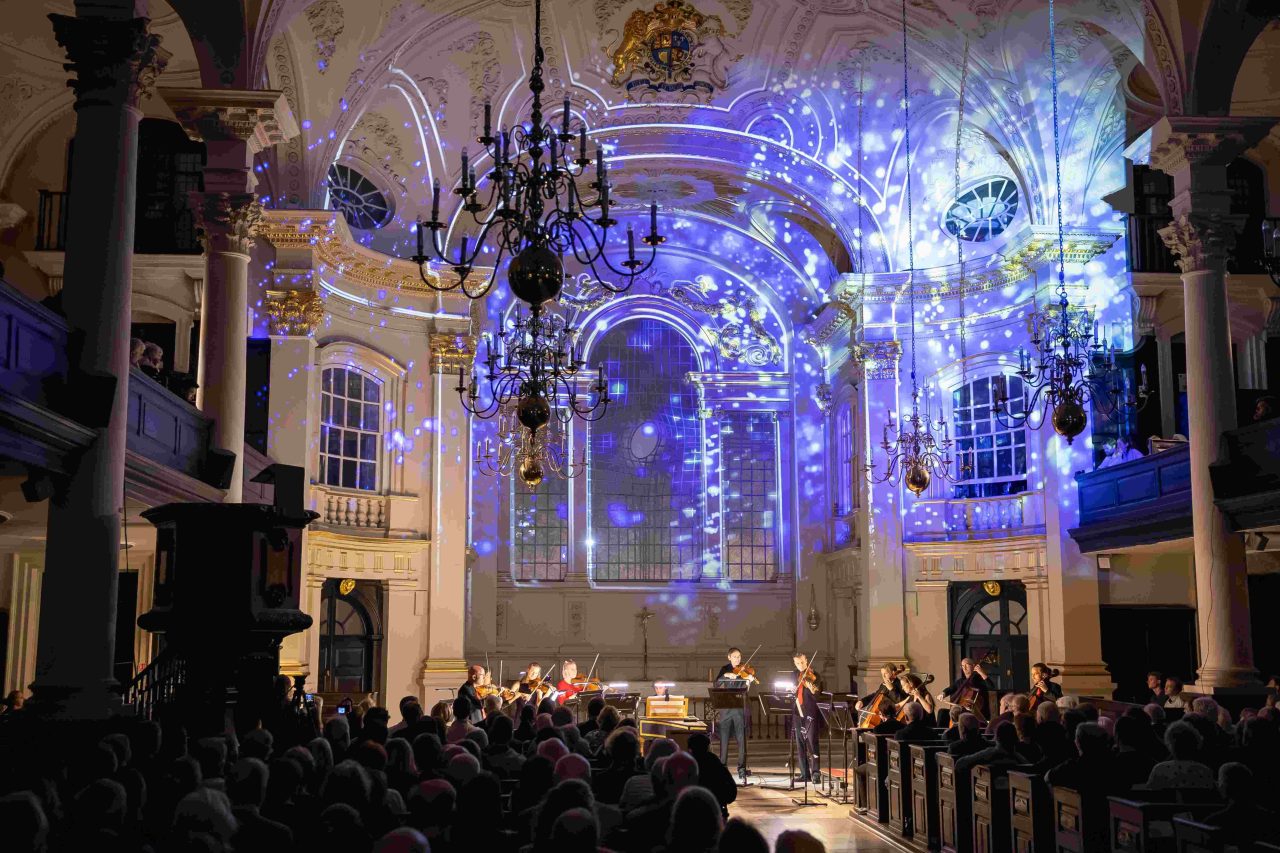 Beautiful patterns are projected on the back wall of a church, over the heads of musicians.