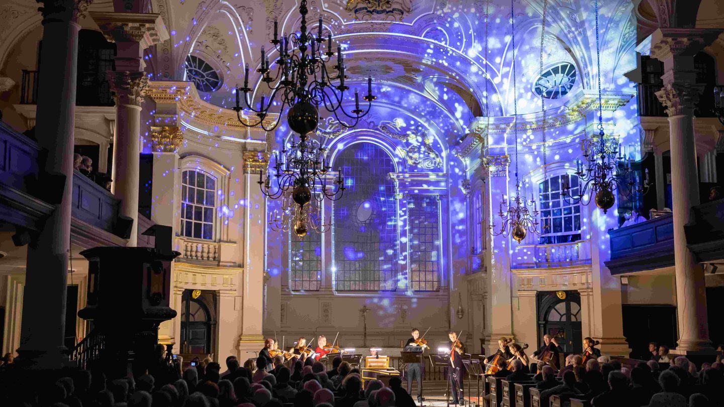 Beautiful patterns are projected on the back wall of a church, over the heads of musicians.