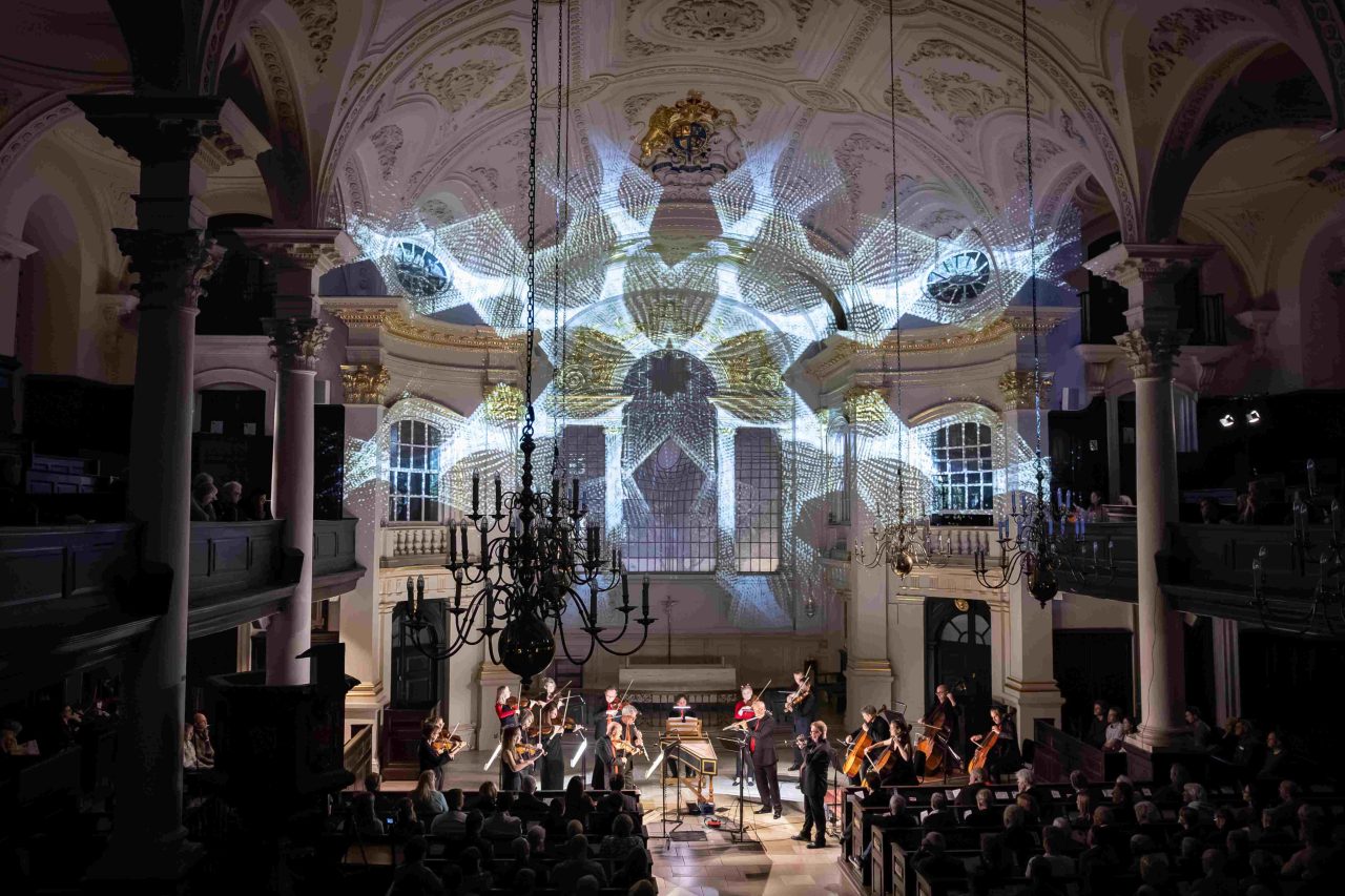 Beautiful patterns are projected on the back wall of a church, over the heads of musicians.