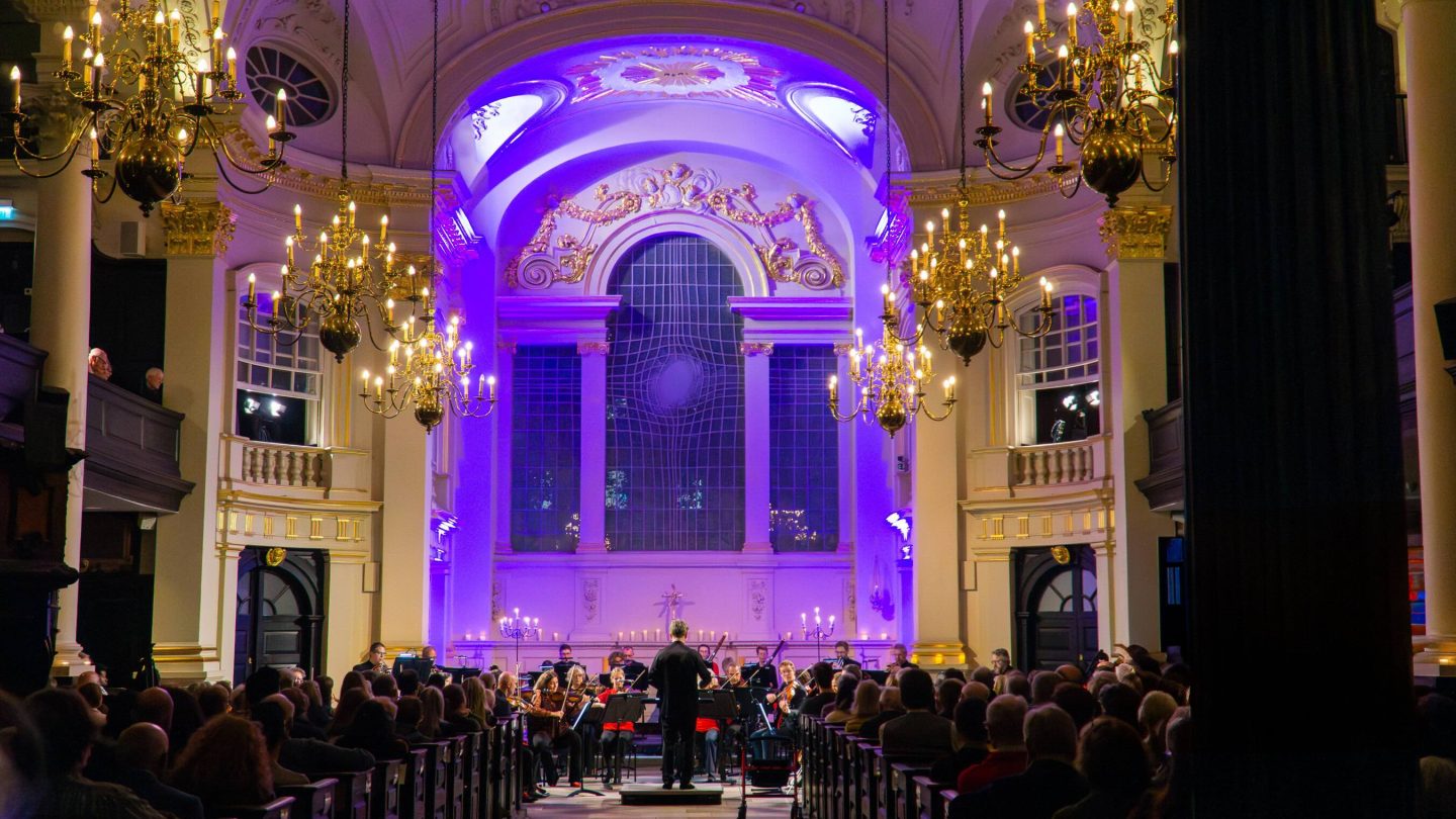Attractively lit church with orchestra seated at far end.