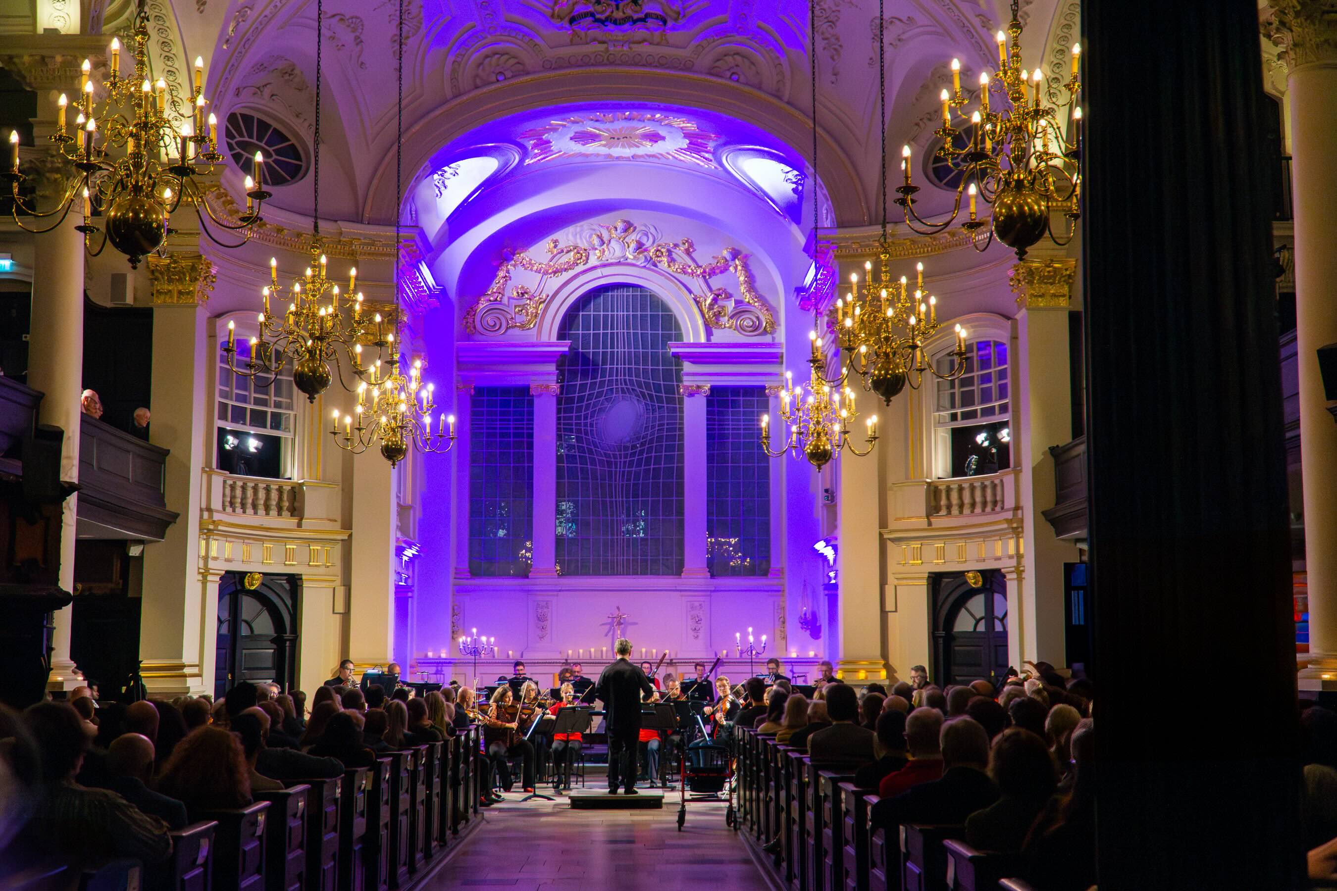 Attractively lit church with orchestra seated at far end.