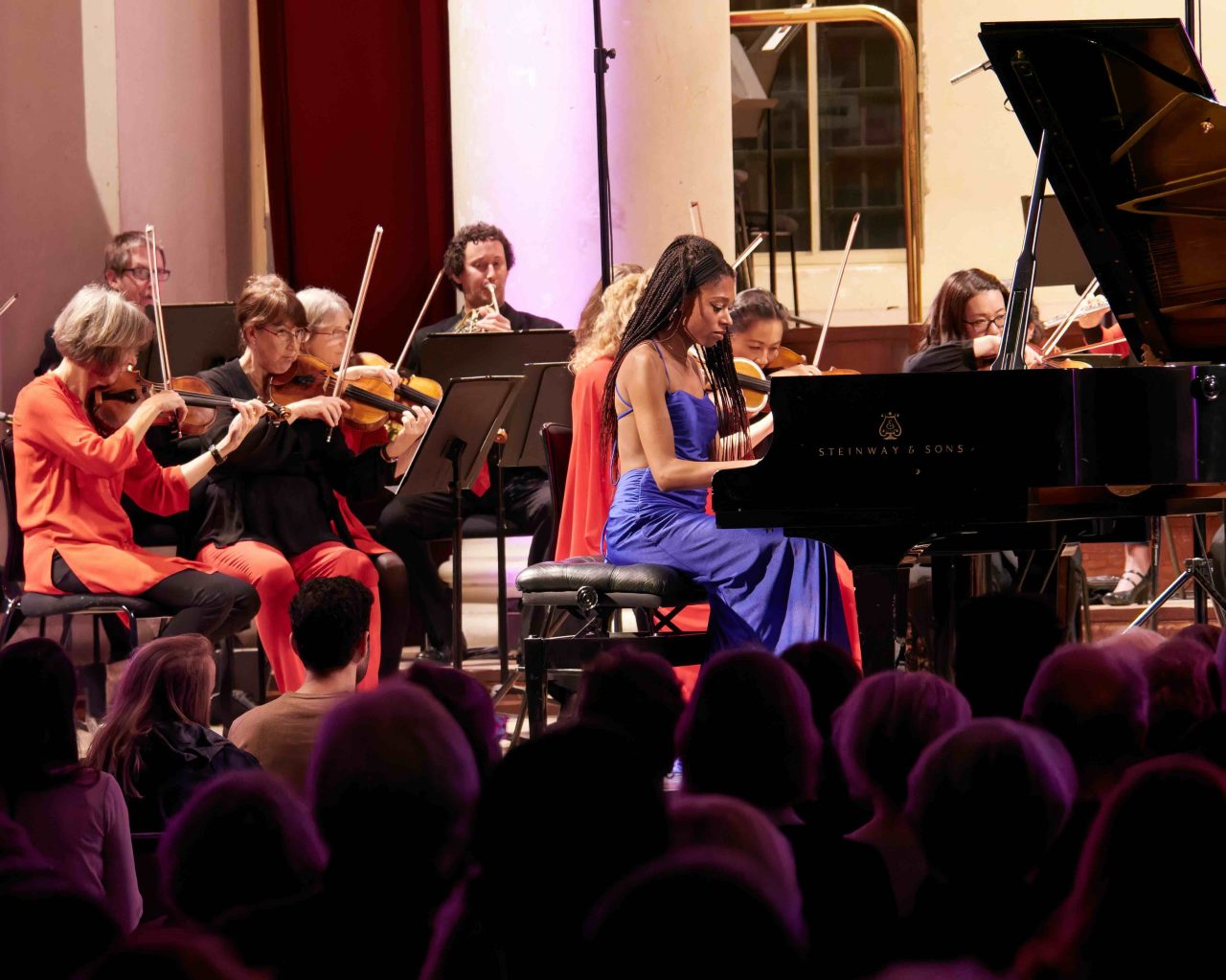 Woman plays piano alongside orchestra.