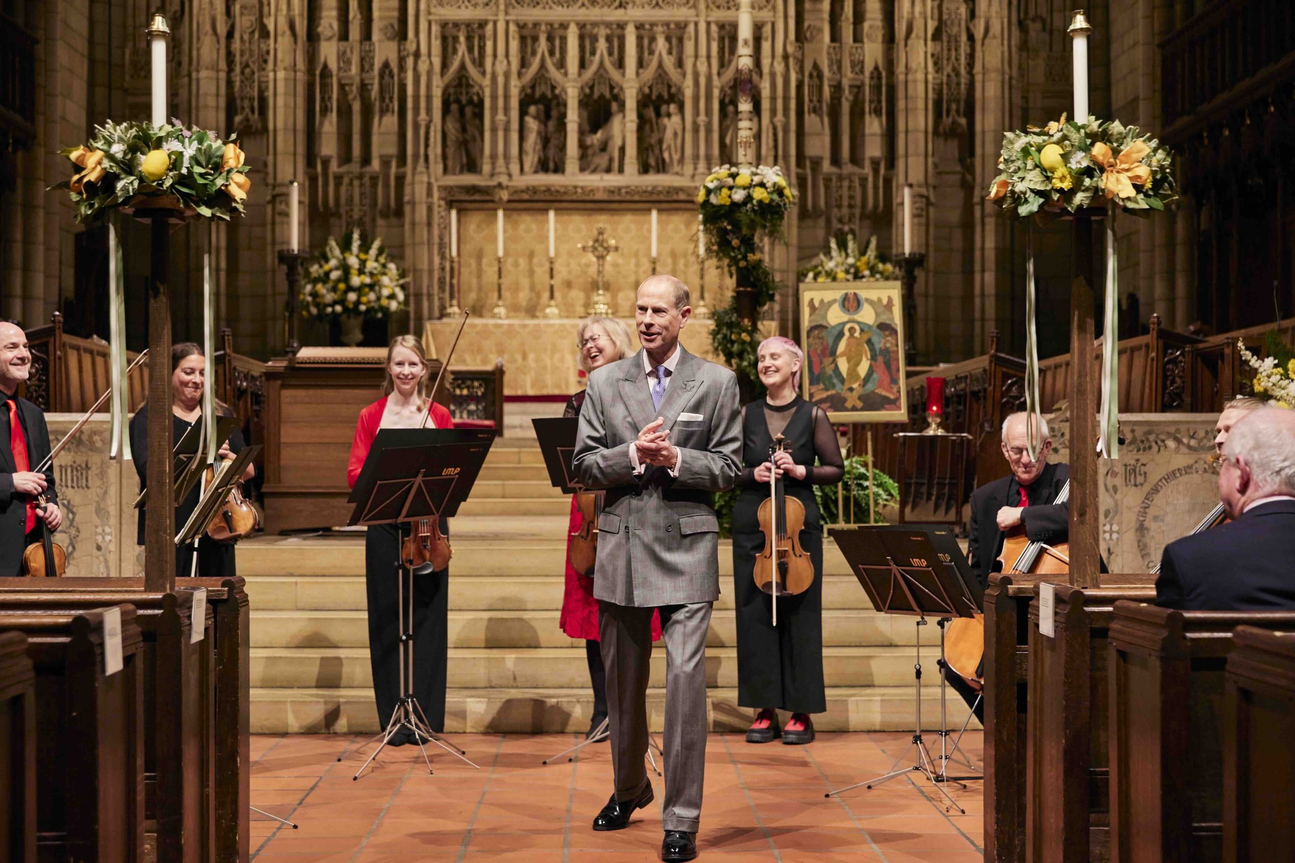 Prince Edward speaks with musicians stnading behind him with their instruments.