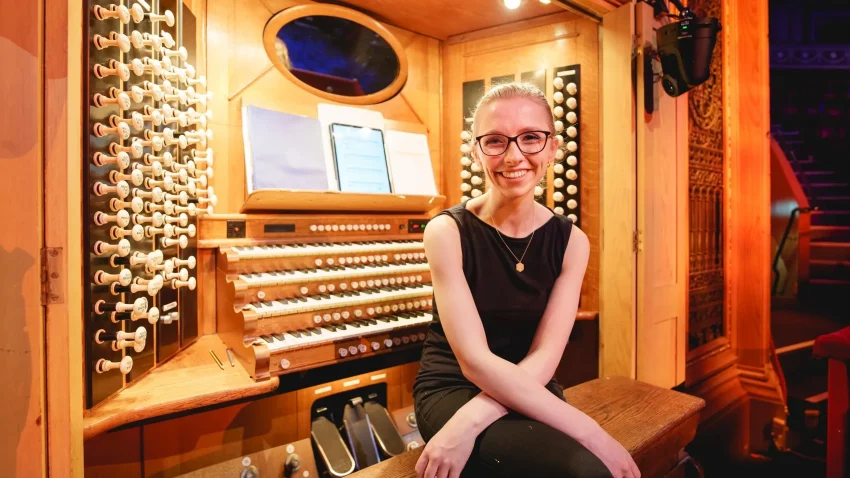 Smiling woman sits in front of an organ console.