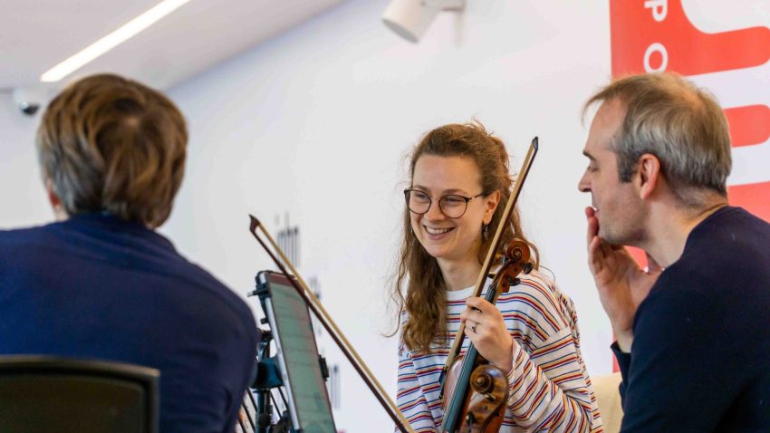 A woman holding violin smiles next to other musicians.