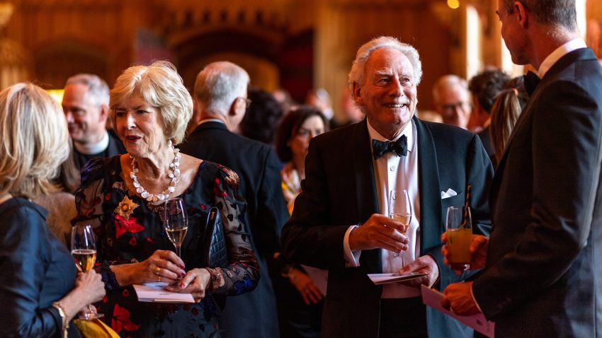 Guests in black tie socialise in a grand building, holding champagne flutes.