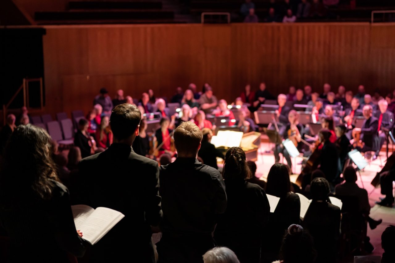 A group of singers standing in a line in the aisles of a concert hall holding sheet music.