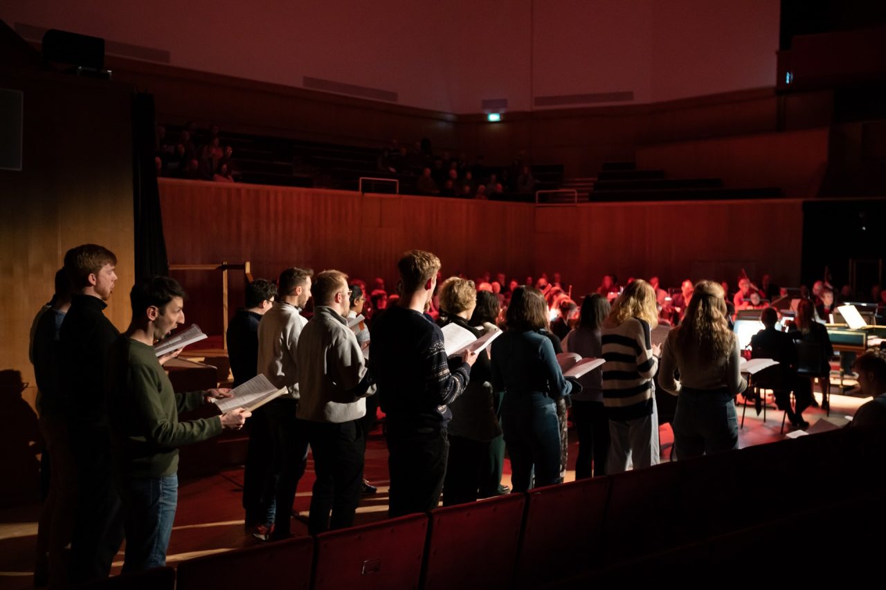 A group of singers stand behind one another.