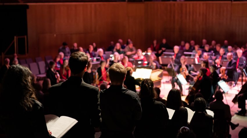 A group of singers standing in a line in the aisles of a concert hall holding sheet music.