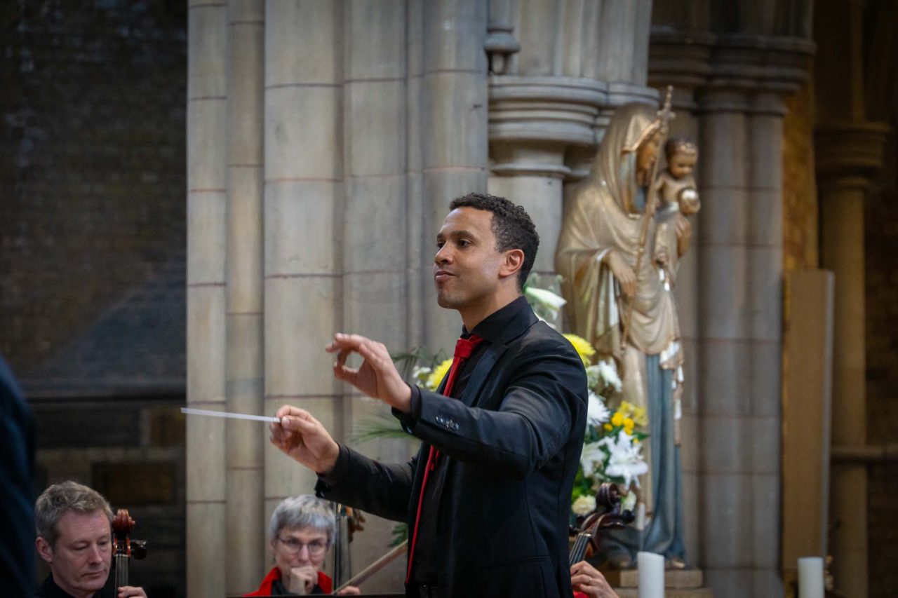 A man holds a baton and raises it to conduct.