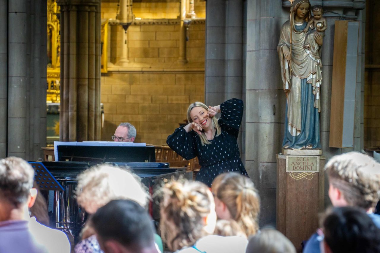 A woman in a spotty top playfully holds her hands to her face to mimic an animal.