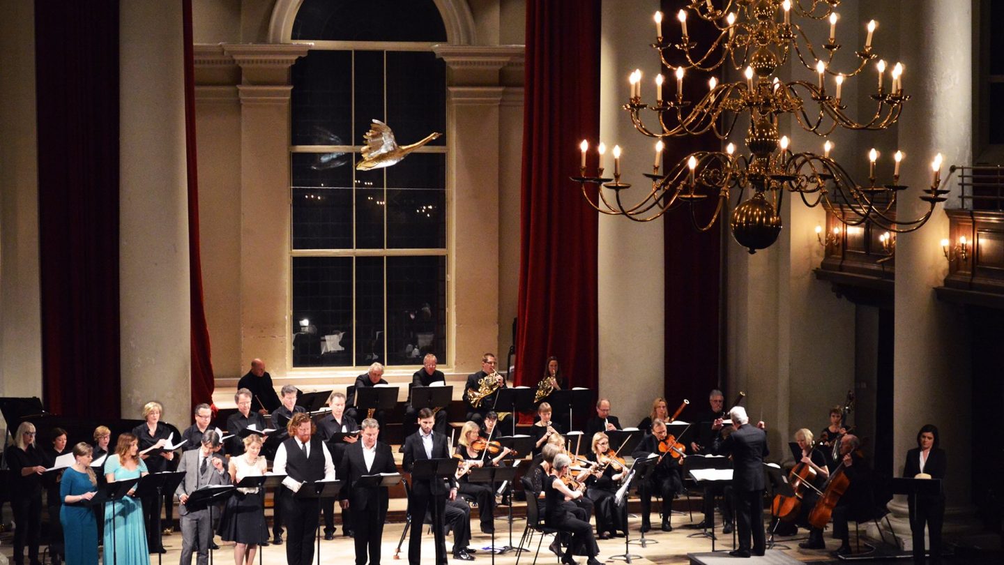 A model of a golden goose hangs above orchestra and singers on stage.