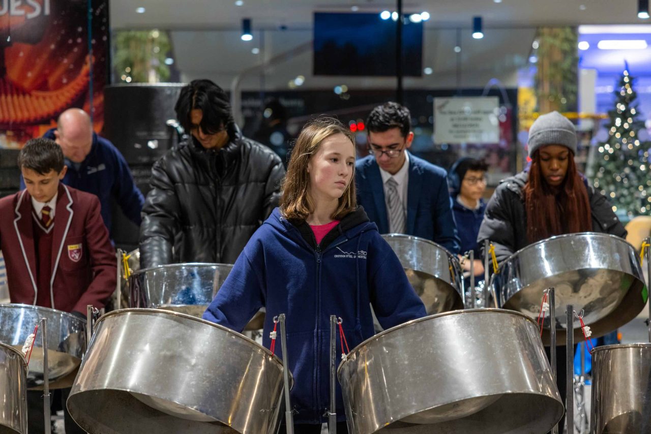 A young girl plays two steel pans.