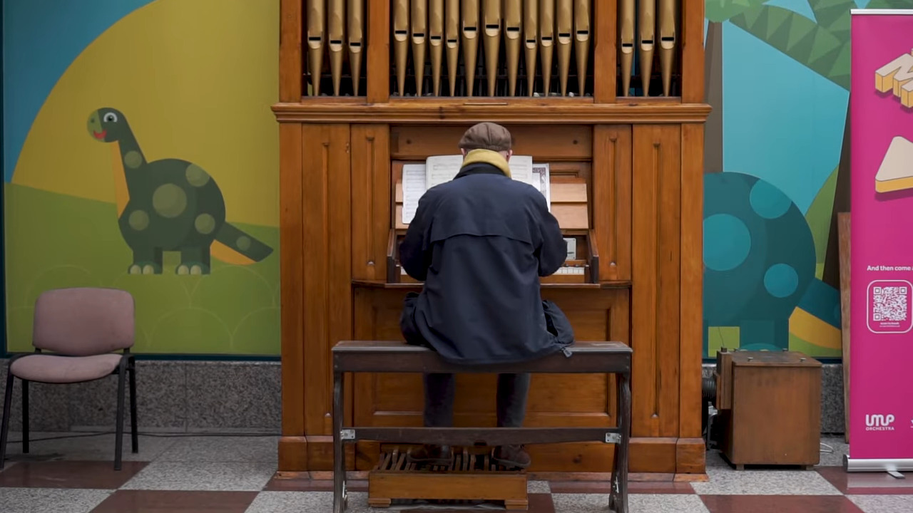A man sits down on a bench playing a pipe organ.