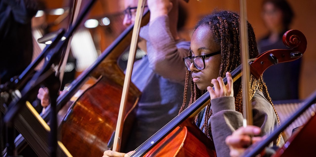 A girl wearing glasses plays the cello.