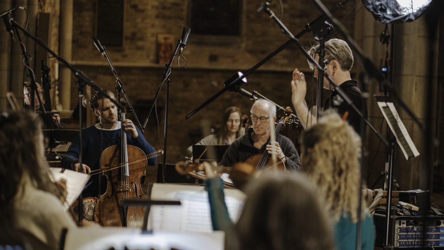 A group of a musicians and a conductor play together in front of microphones.